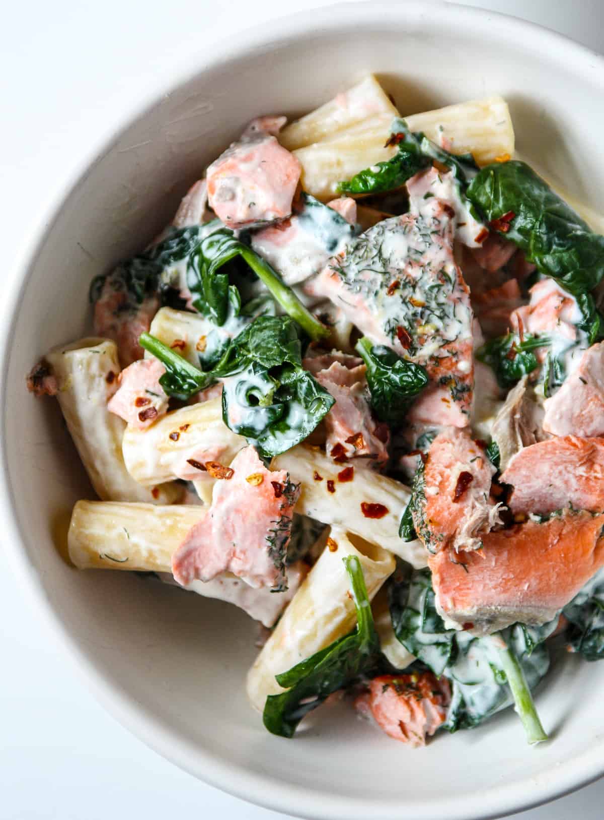 Pasta with salmon and spinach in a white bowl.