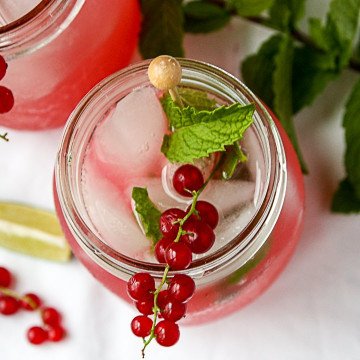 A drink garnished with red berries and a mint leaf