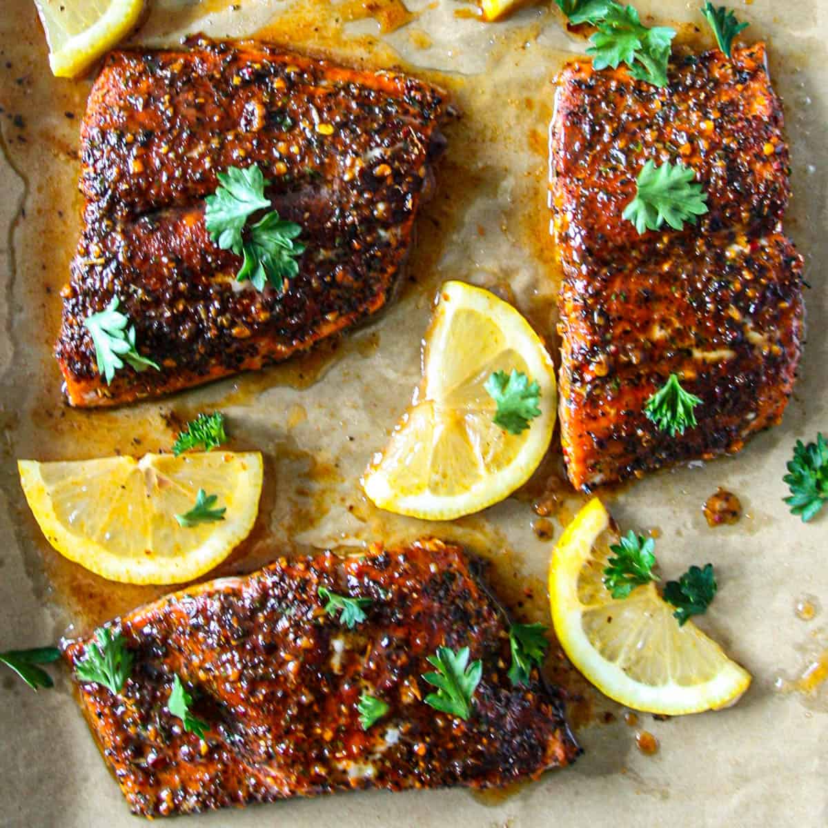 Three Cajun honey butter salmon fillets on a baking sheet with lemon wedges.