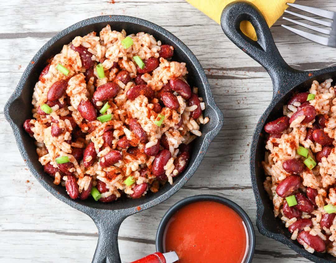 Red beans and rice in small black skillet with a small dish of hot sauce.