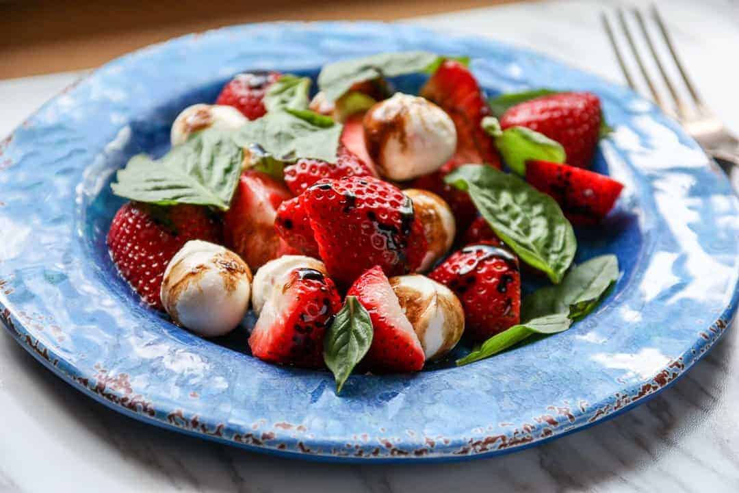 Salad with mozzarella balls and sliced strawberries on blue plate.