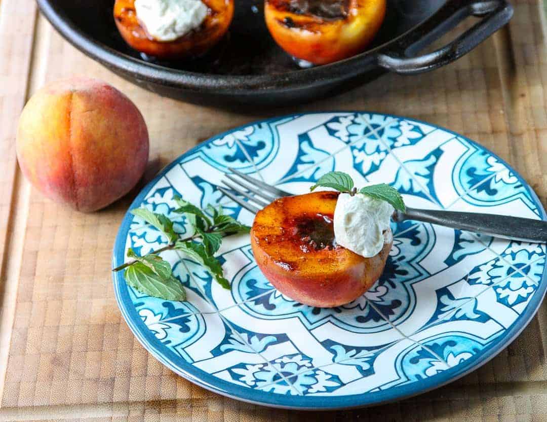 A grilled peach on a plate, with a fork