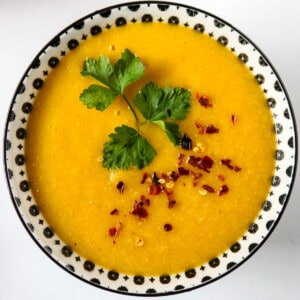 Overhead view of a bowl of carrot soup garnished with cilantro and chili flakes.