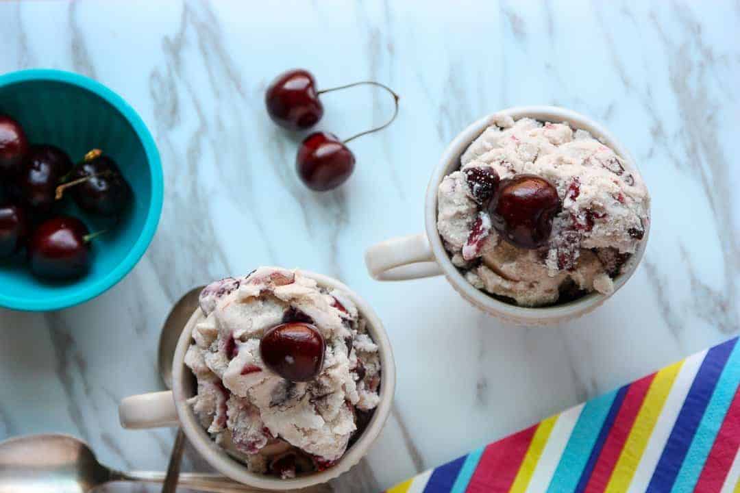Two dishes of ice cream next to a bowl of cherries.