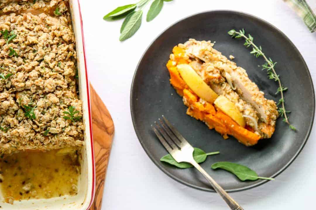 slice of casserole with layers of sweet potato, apple, and turkey on a black plate with a sprig of thyme and sage leaves