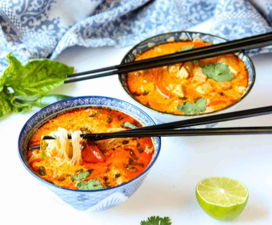 red thai curry chicken soup in two blue & white bowls with black chopsticks