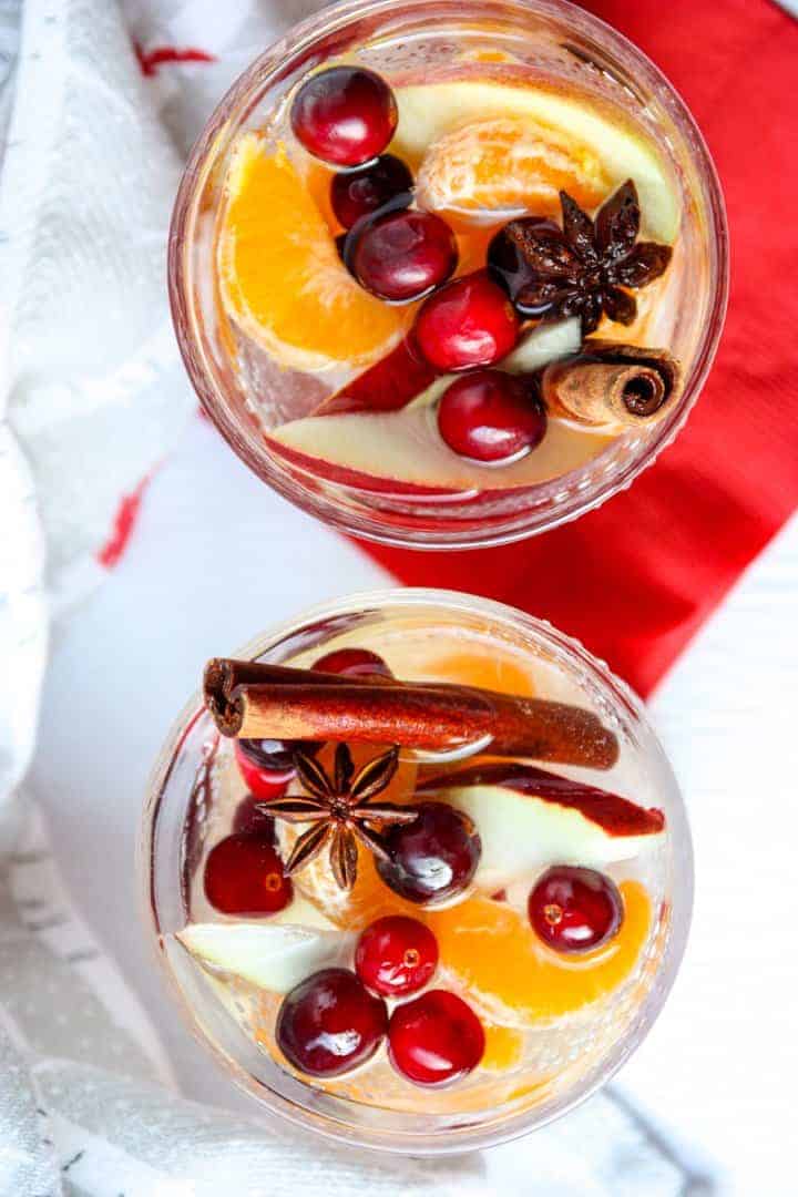 Top down view of two glasses of sangria filled with cinnamon sticks, apple slices, orange slices, and cranberries