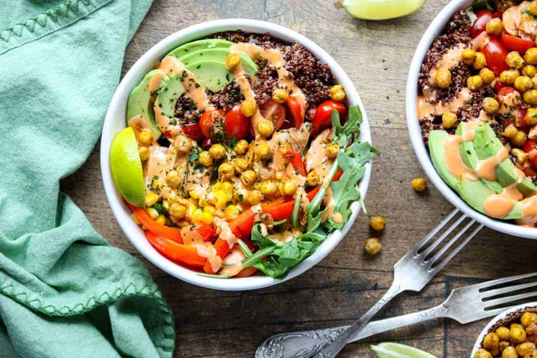 Two white bowls filled with quinoa and vegetables on a wooden table