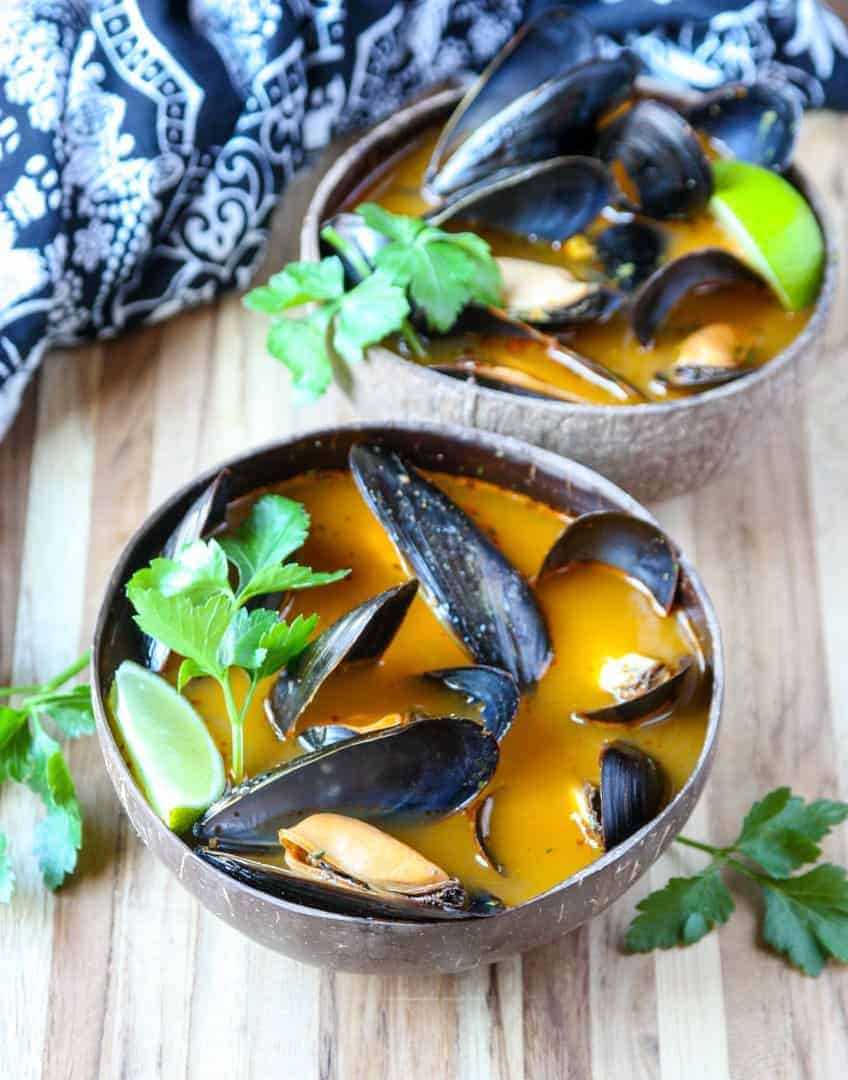 Mussels thai style in orange broth in brown wooden bowl on wooden table