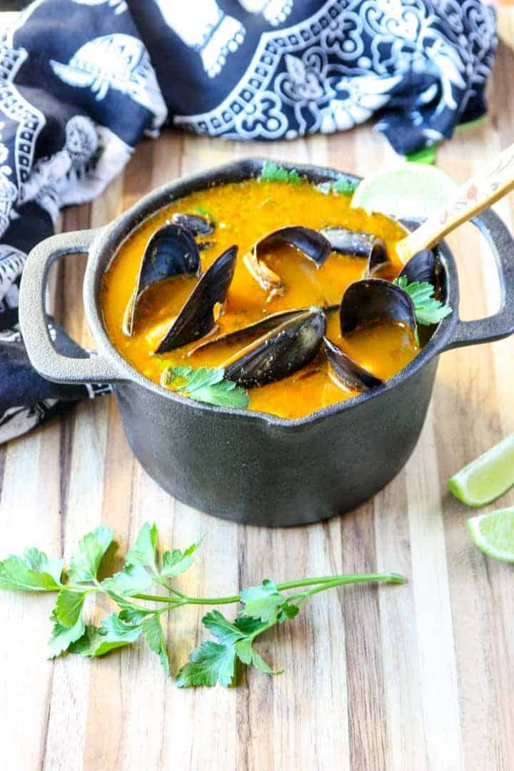 A pot of mussels thai style in orange broth on wooden table