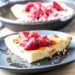 A slice of Dutch baby pancake topped with strawberries on a black plate.