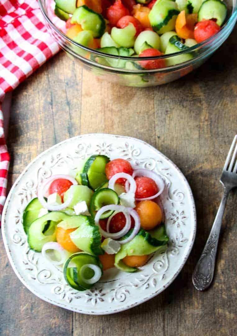 A bowl of food sitting on top of a wooden table, with Salad and Cucumber