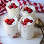 Four jars of mousse on a table, with raspberries