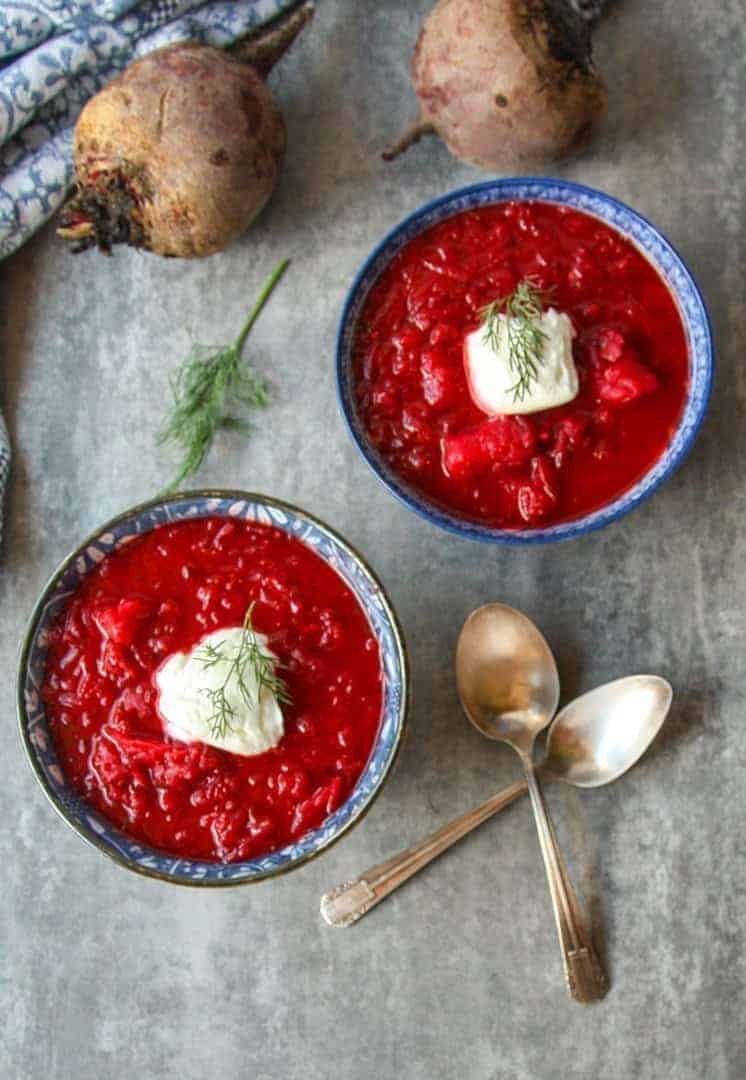 top shot of red beet soup in two blue bowls with dollop of sour cream on top