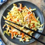 Cabbage stir fry on a black plate with black chopsticks