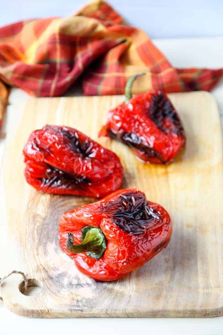 Three roasted red peppers on a cutting board