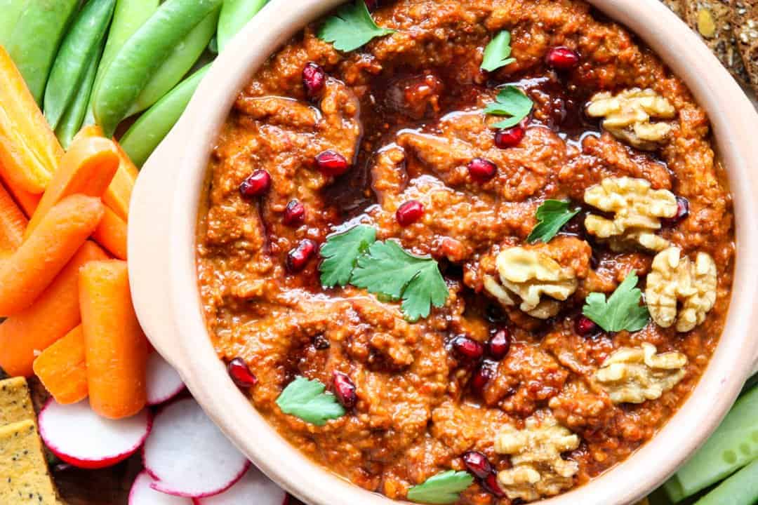 A close up of a bowl of dip topped with walnuts and pomegranate seeds