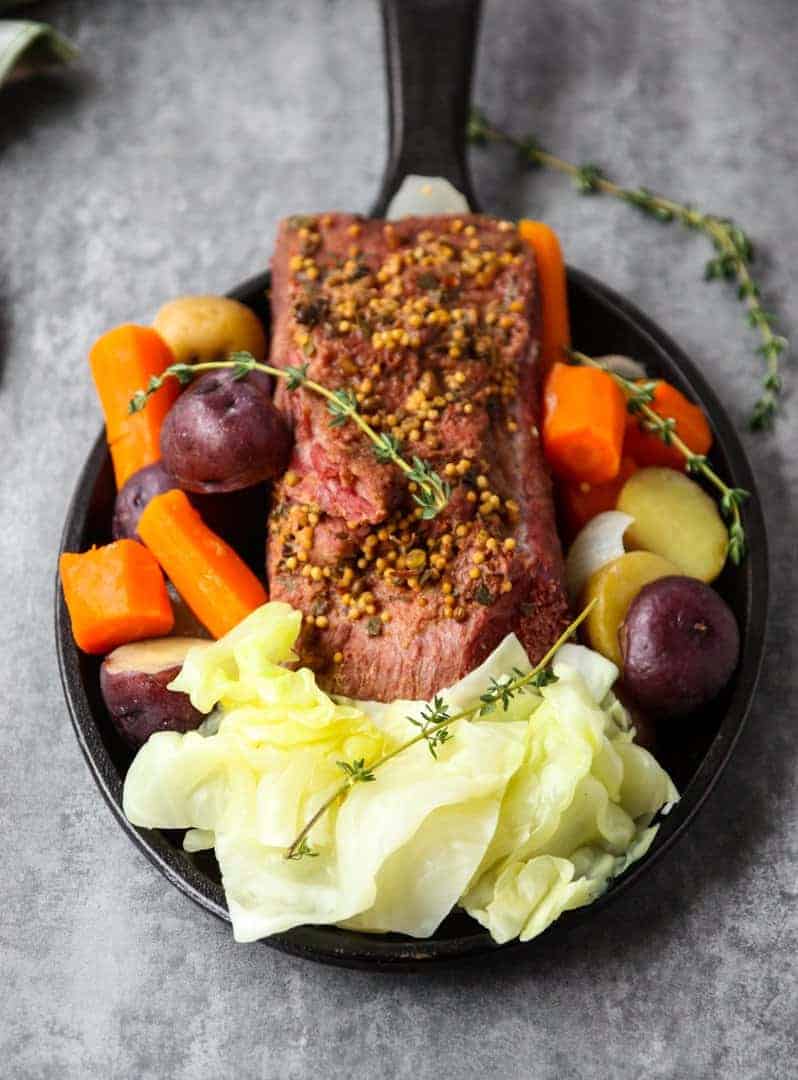 A round black plate of vegetables and slow cooker corned beef and cabbage