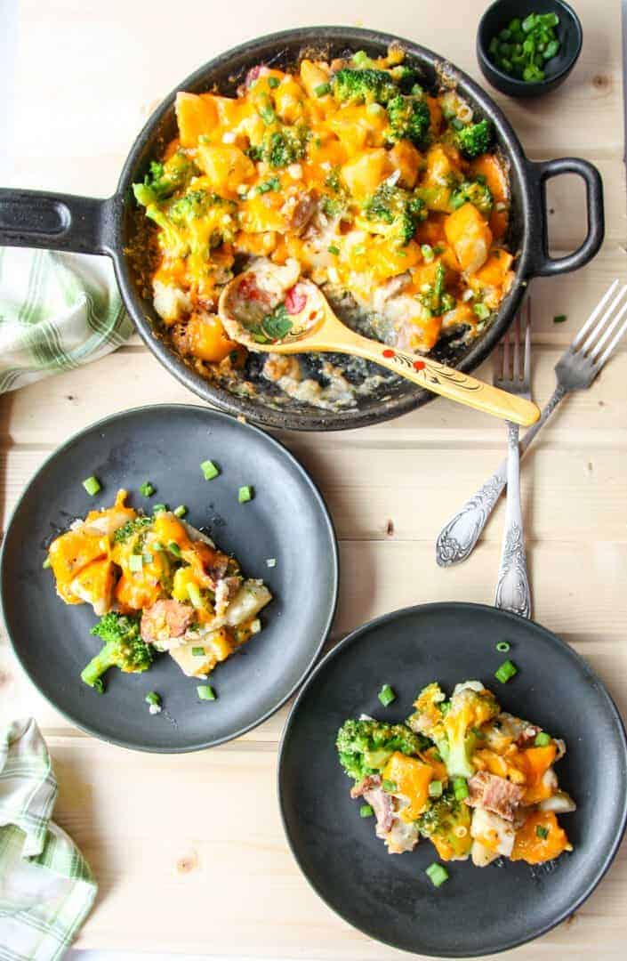 A black plate with cheese, broccoli and potatoes on top.