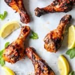 Six grilled harissa chicken drumsticks and lime wedges on parchment paper