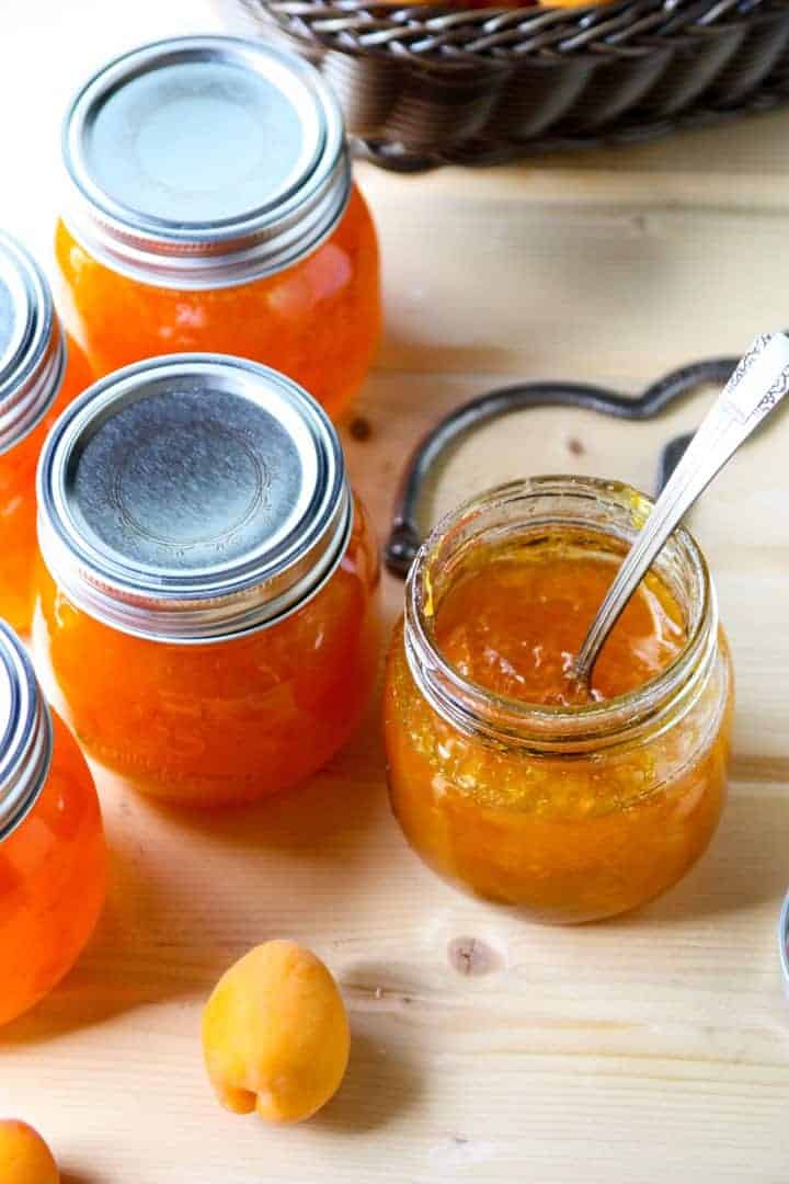 Three jars of apricot jam, two with lids on and one with lid off and a spoon inserted