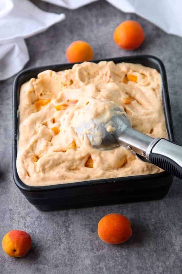 Apricot Mascarpone Ice Cream in a square black dish with an ice cream scoop