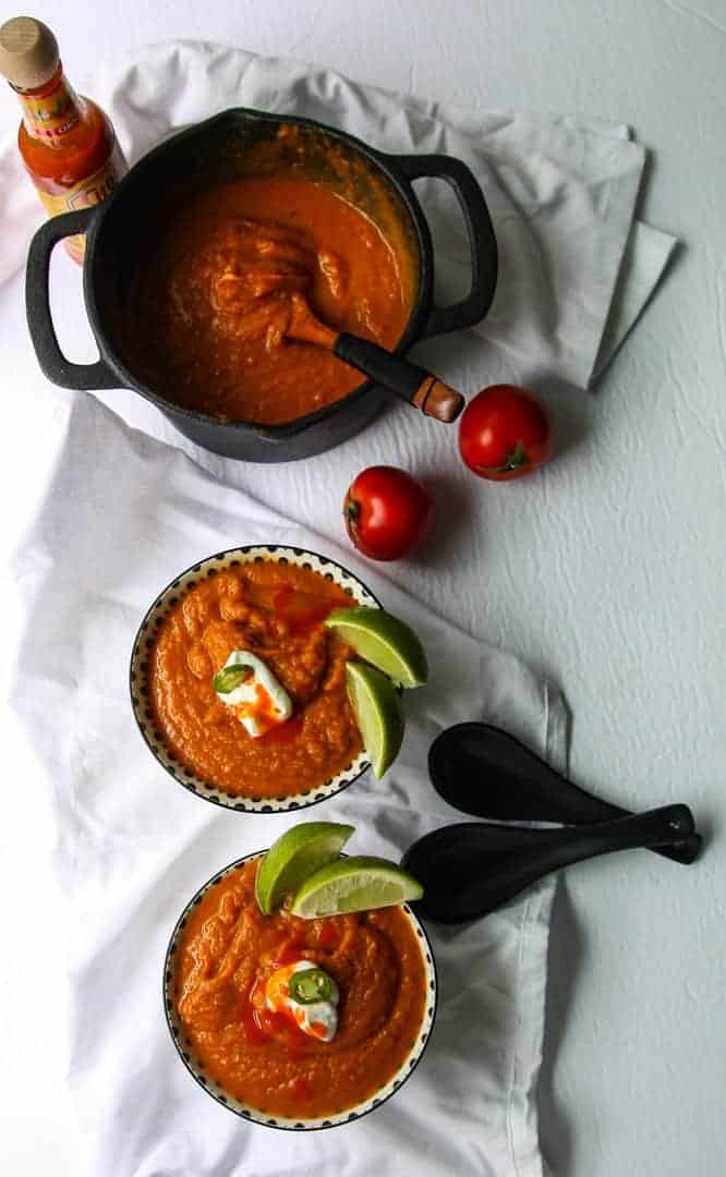 A pot of soup on a table with two bowls of pumpkin soup