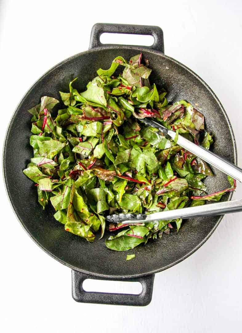 Beet Greens are sautéed in a pan with tongs.