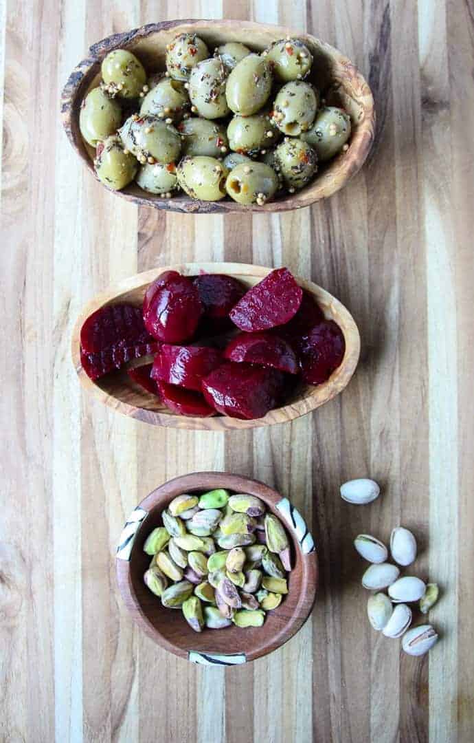 Small dishes of nuts, olives and pickles on a wooden cutting board