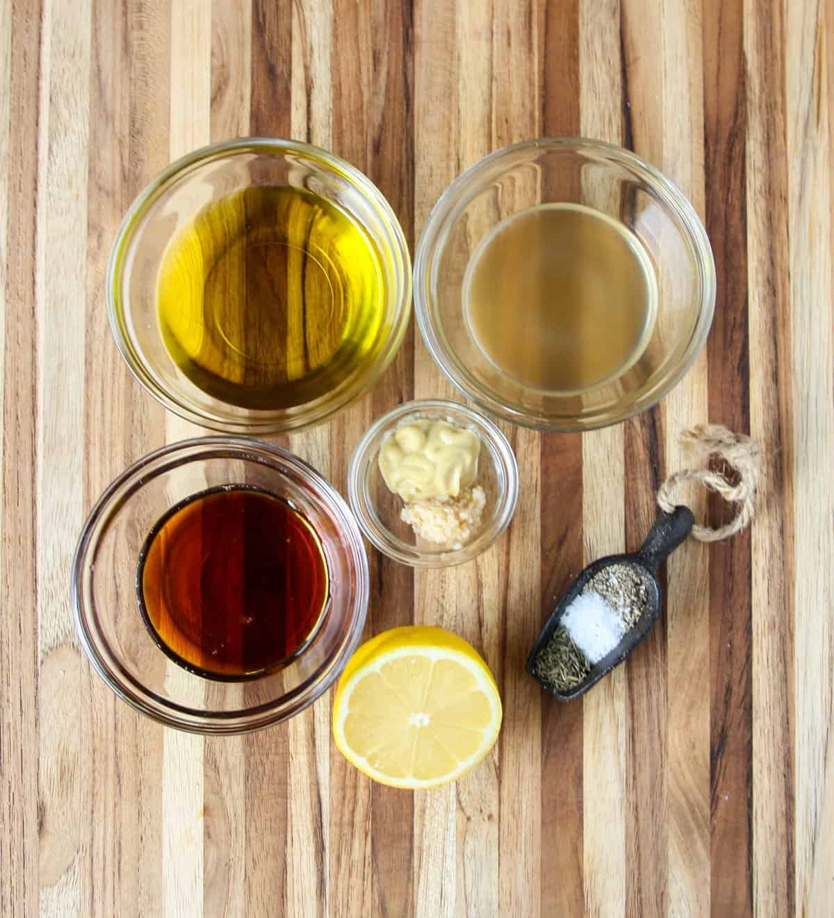 Ingredients to make salad dressing in glass bowls on a wooden cutting board.