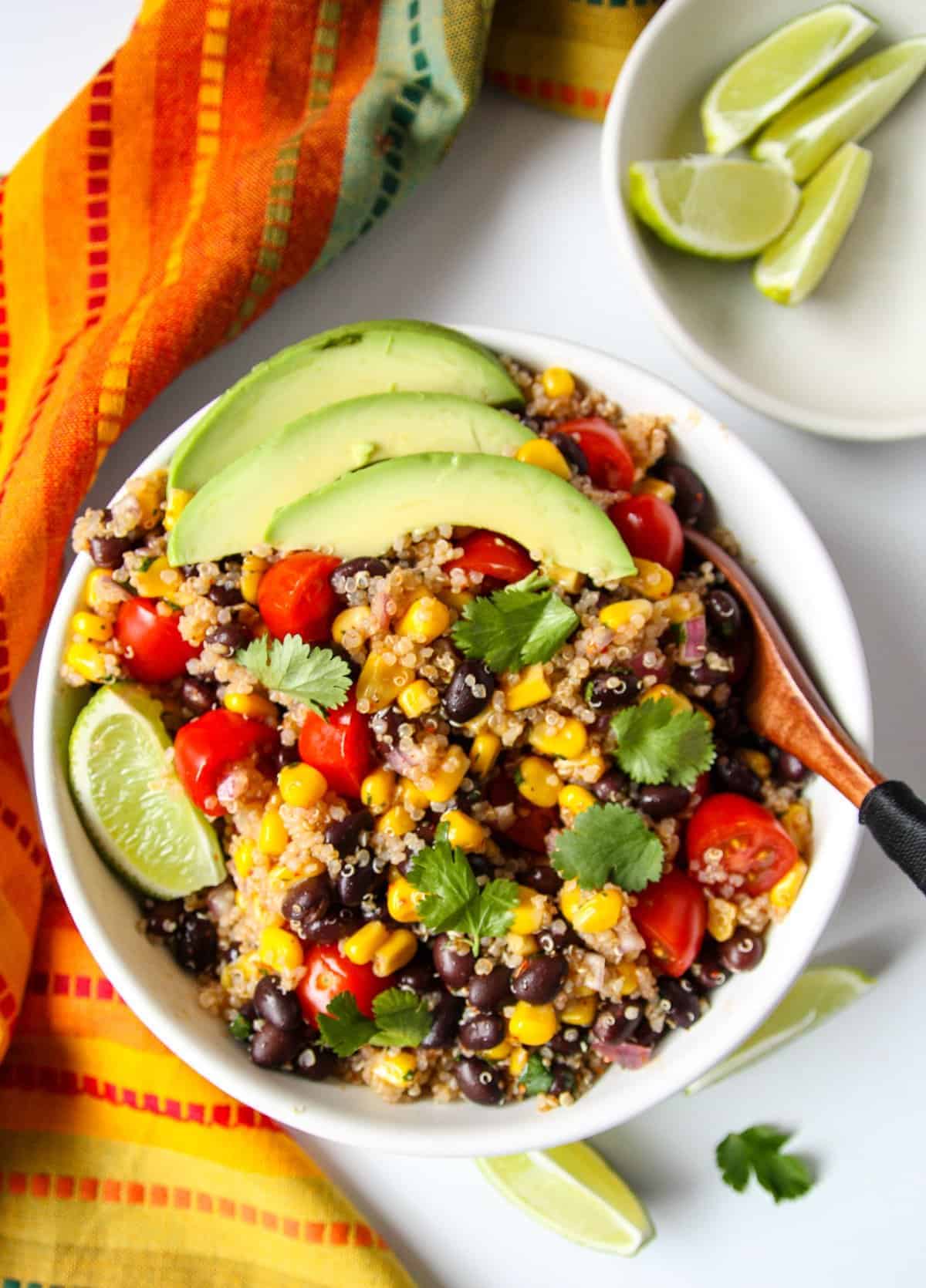 Southwestern quinoa salad in a white bowl topped with avocado slices.