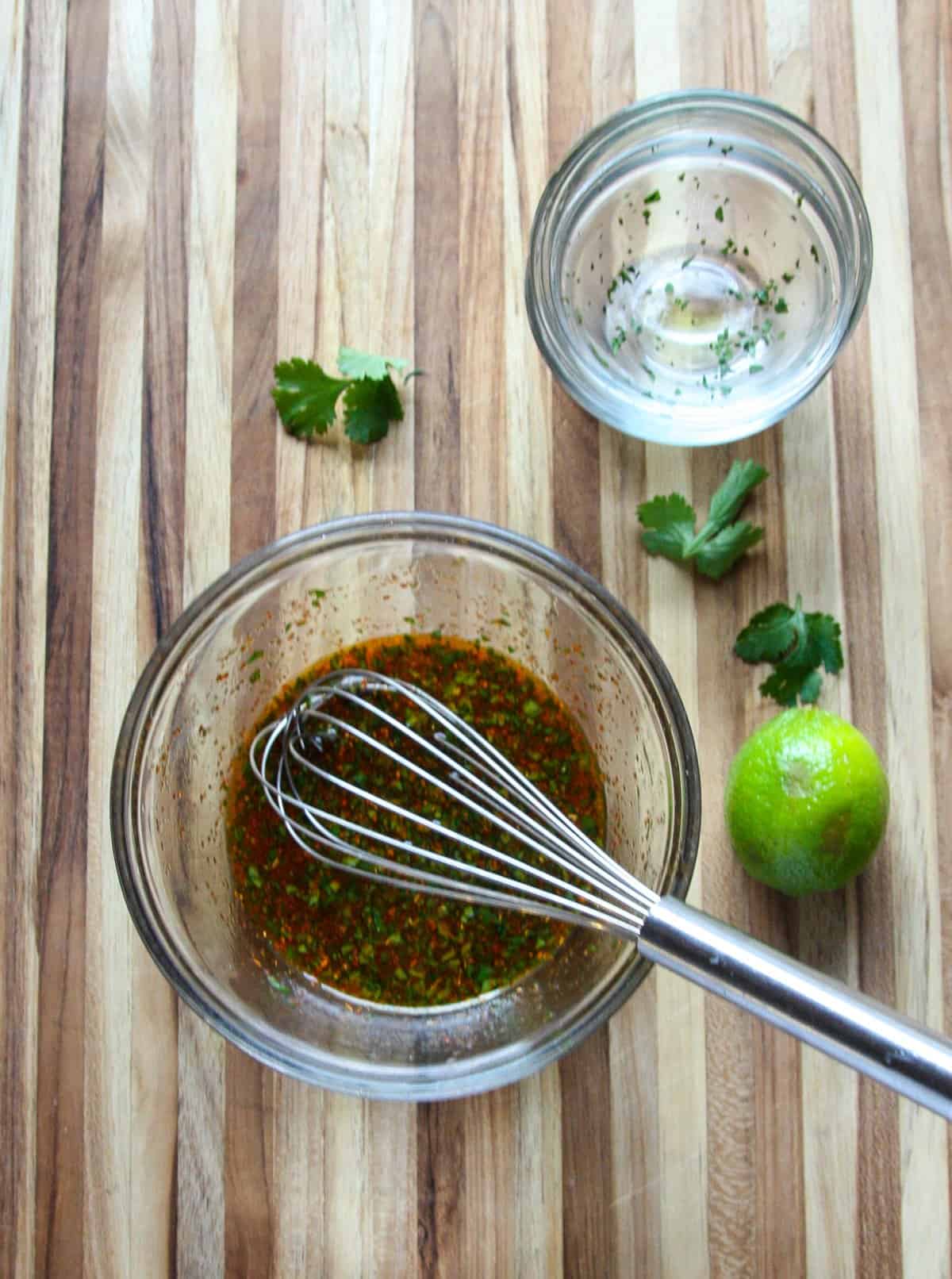 Dressing ingredients being whisked together in a glass bowl.