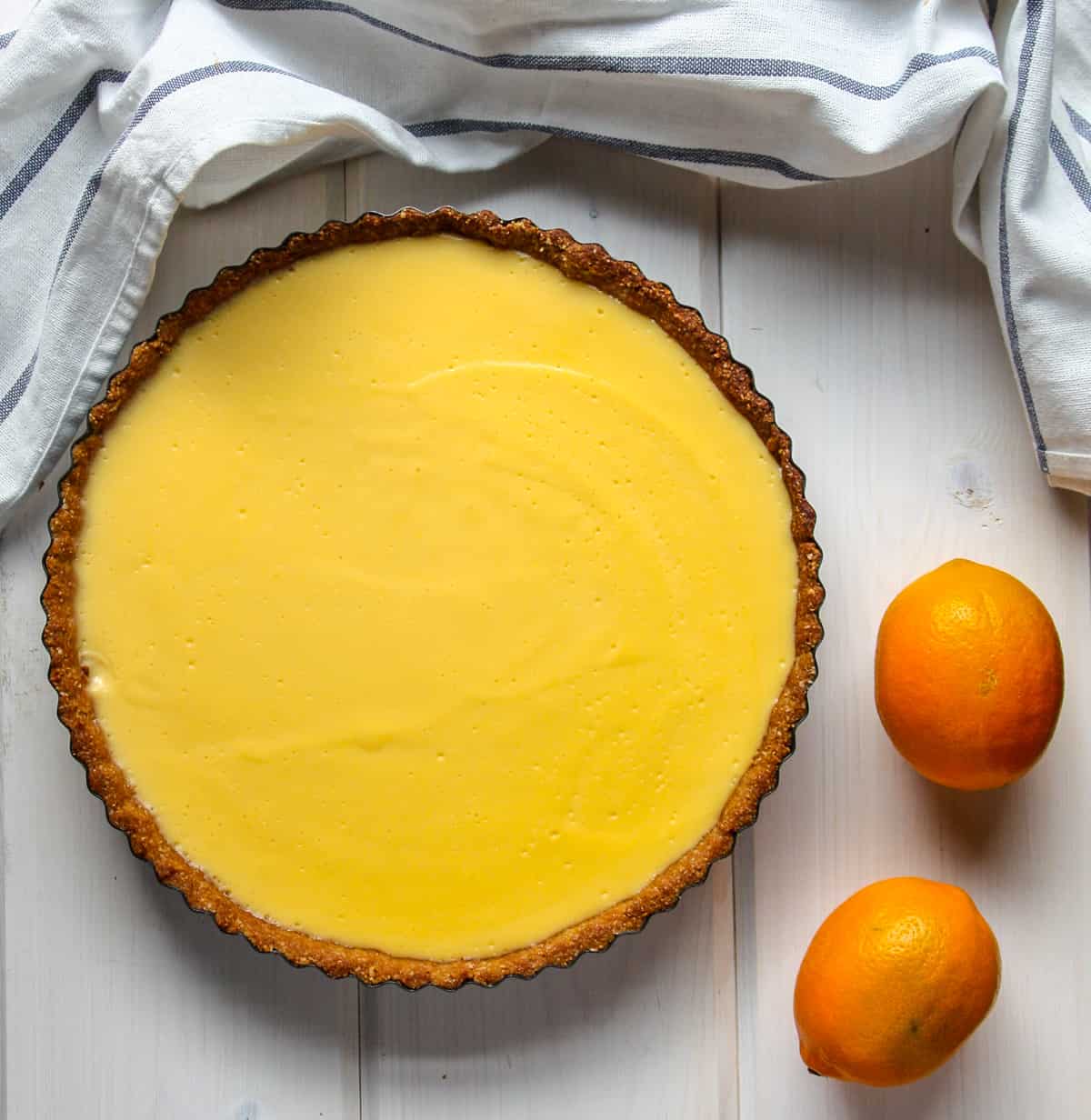 A lemon tart and two lemons on a wooden table.