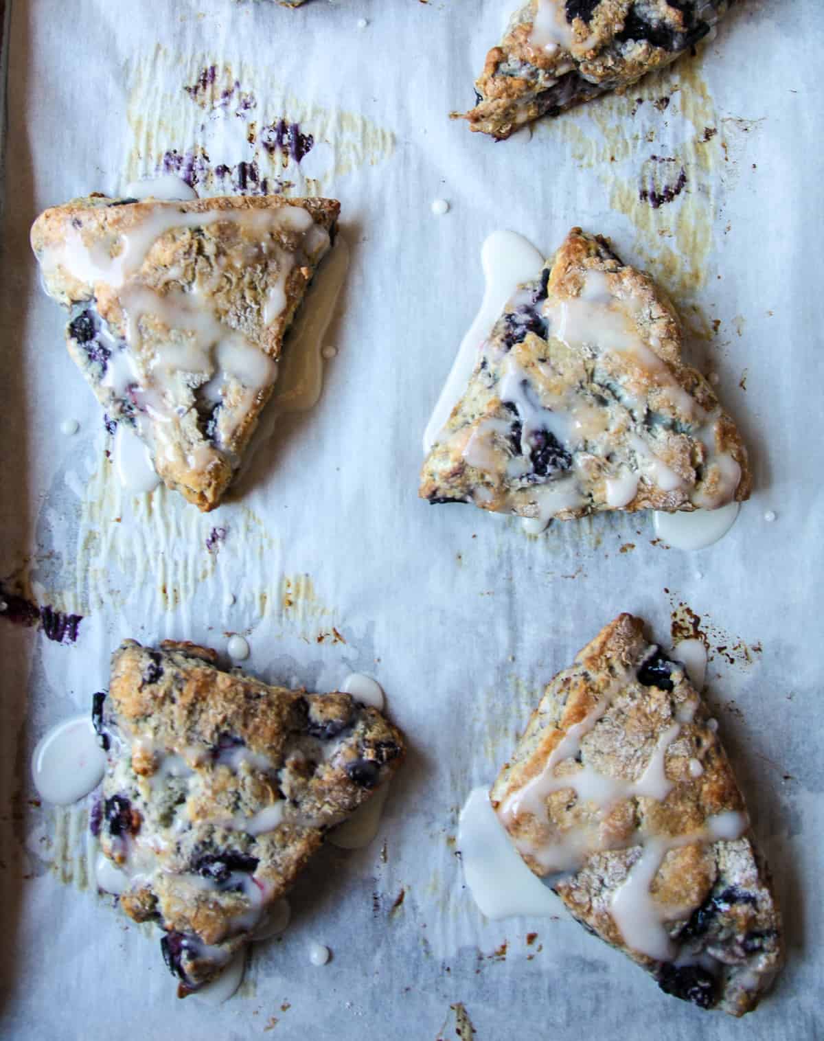 Baked scones drizzled with lemon glaze on a parchment lined baking sheet.