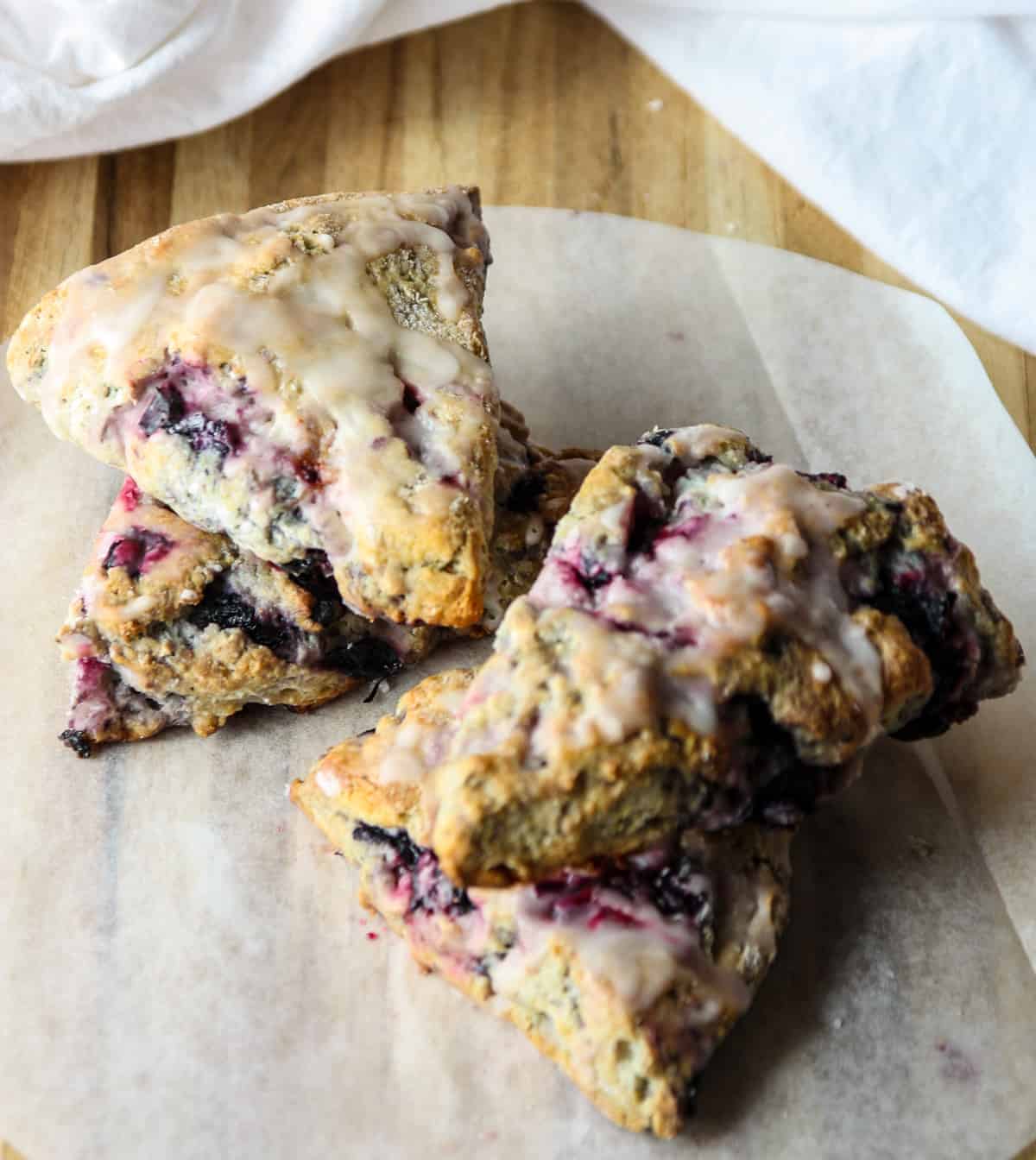 Four glazed blueberry scones on parchment paper.
