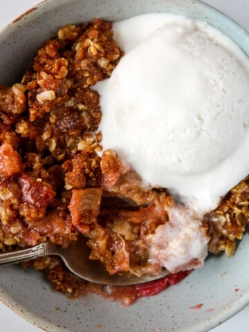 A bowl of rhubarb crisp topped with a scoop of vanilla ice cream.