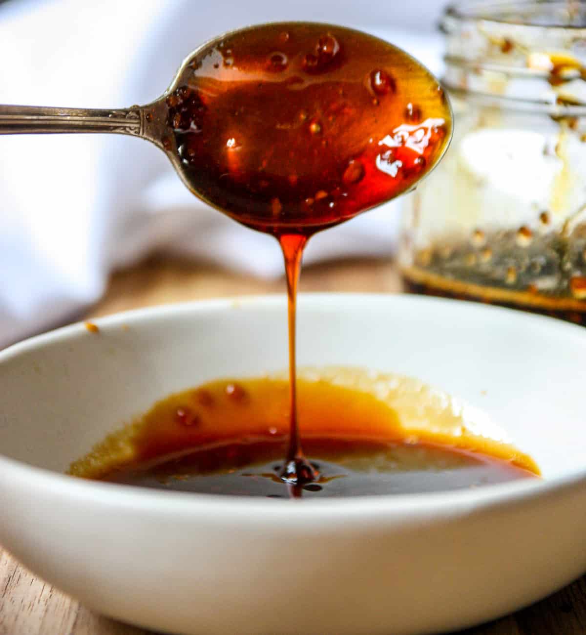 A spoon dripping with honey teriyaki sauce being held aloft over a dish.