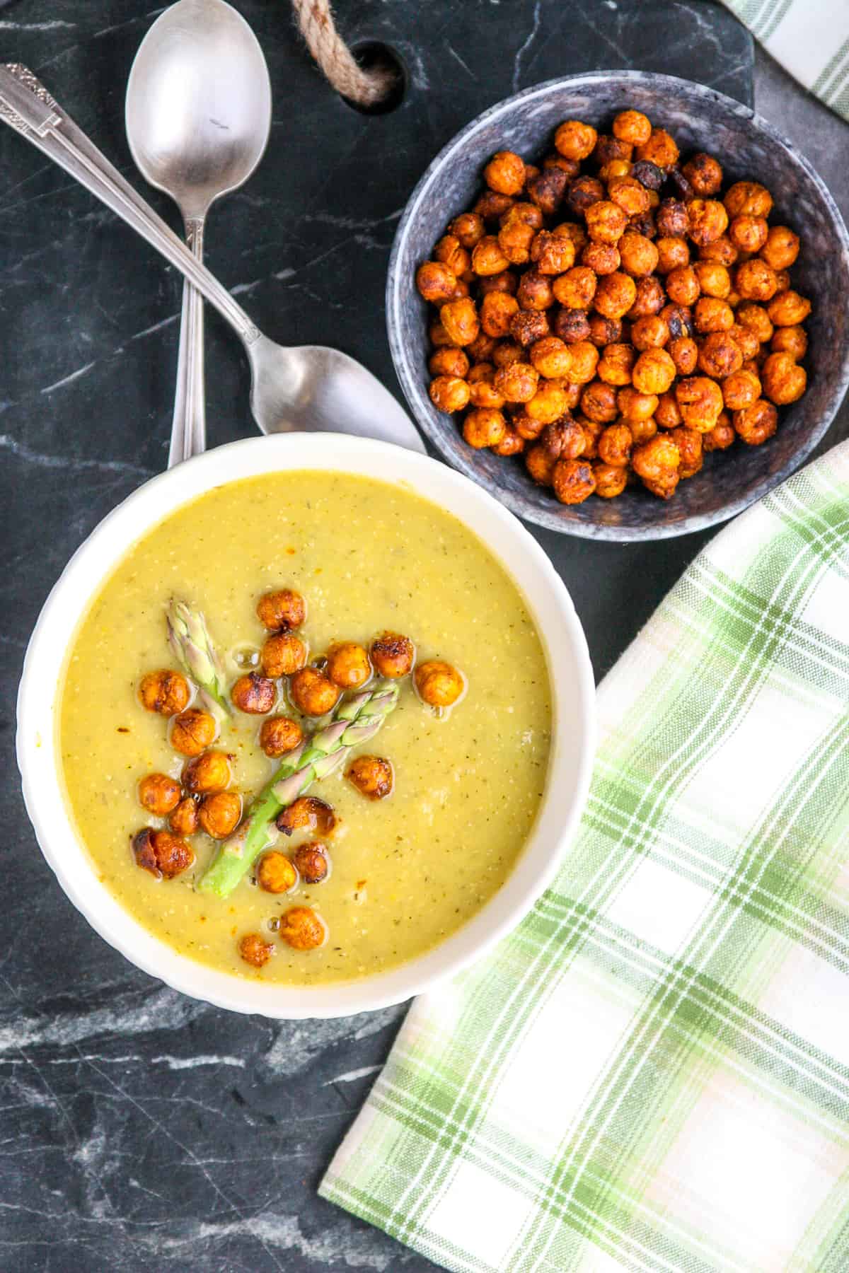 Vegan asparagus soup in a white bowl next to a small black bowl of roasted chickpeas.
