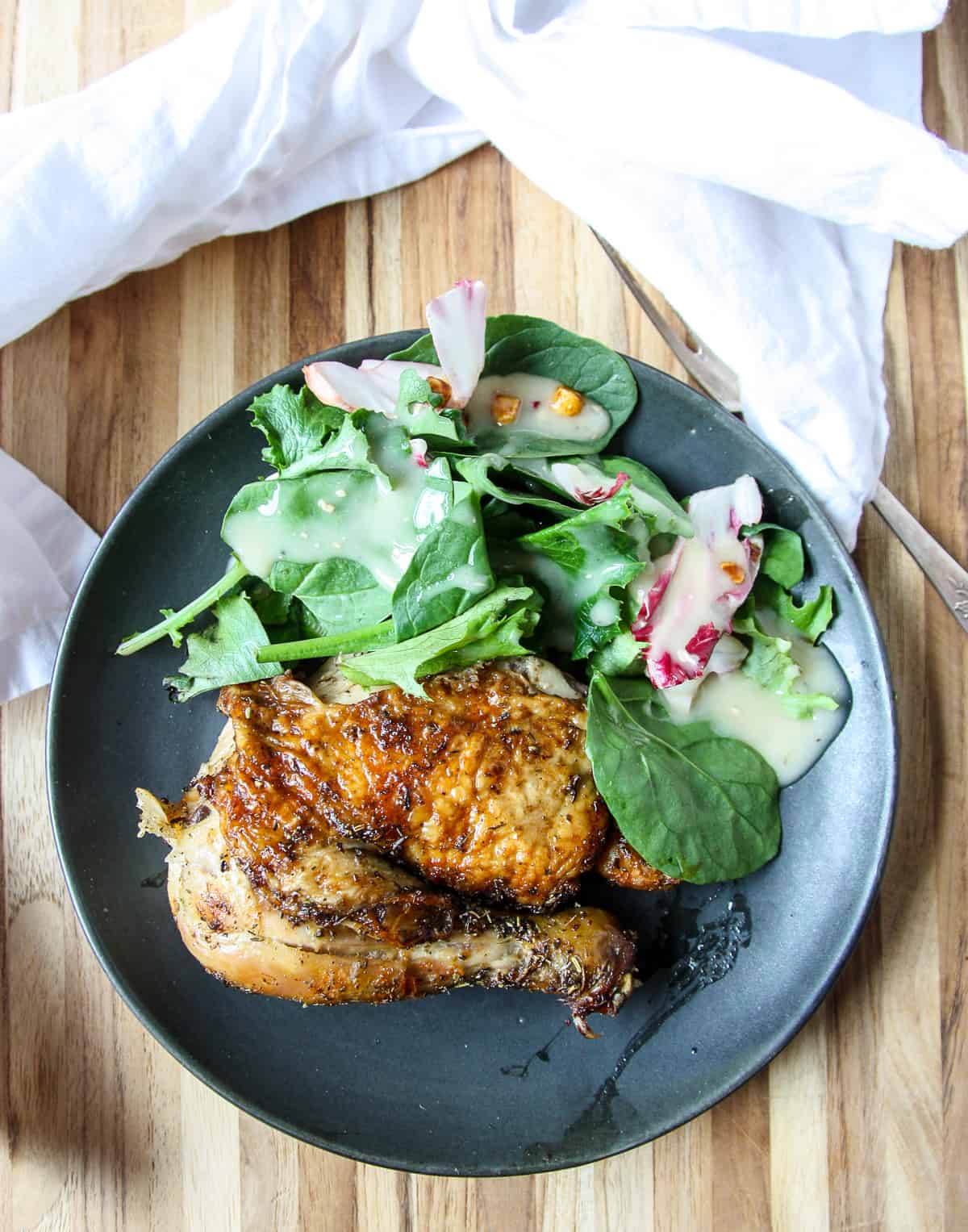 Aleg of roasted chicken on a black plate with salad greens.