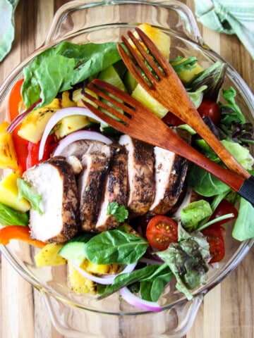 Salad in a glass bowl topped with sliced jerk chicken breast.