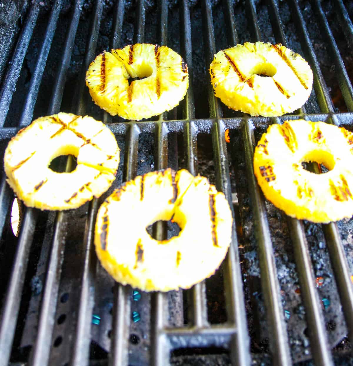 Pineapple slices cooking on a gas grill.