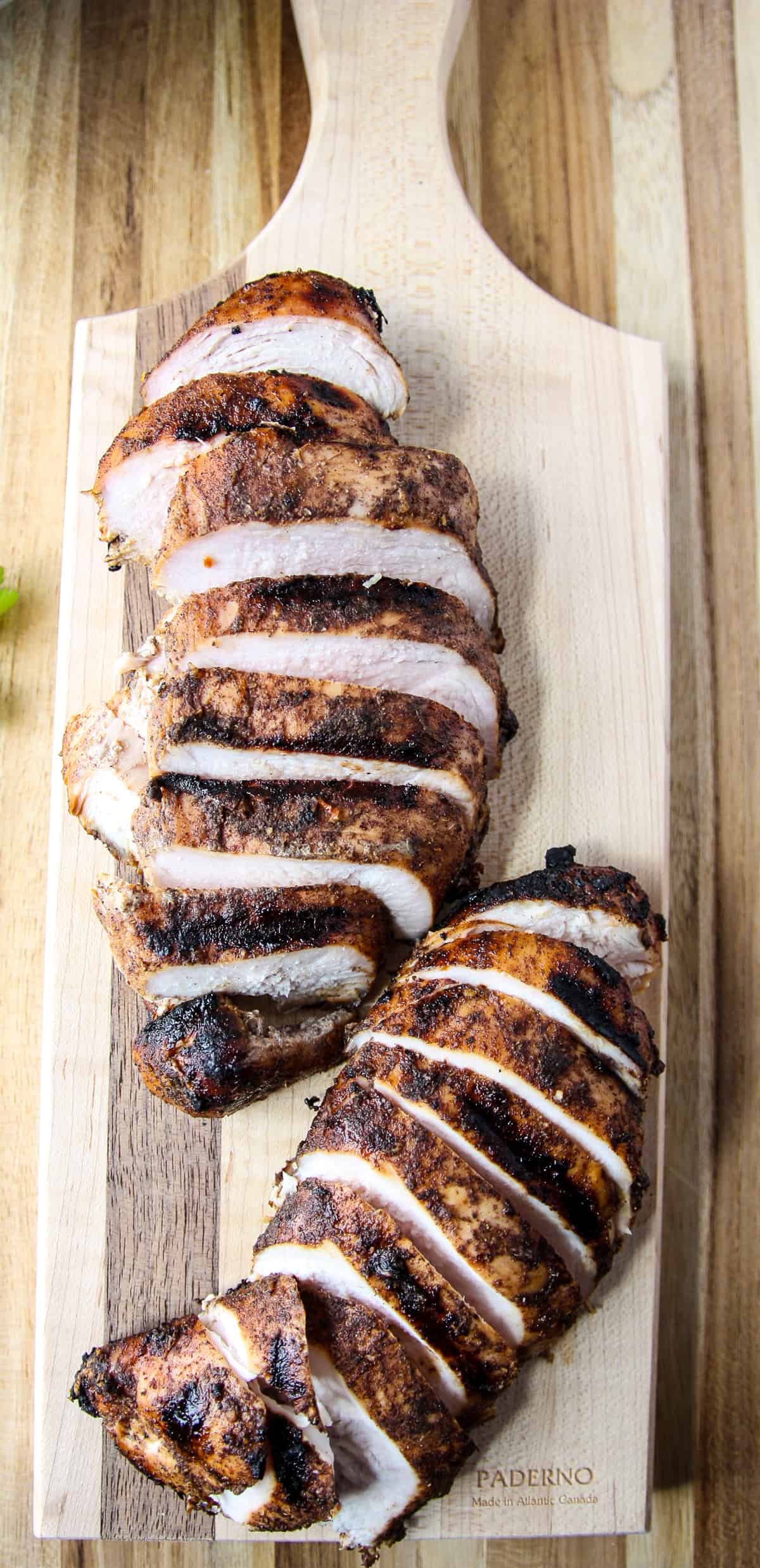 Grilled jerk chicken carved into slices on a wooden cutting board.