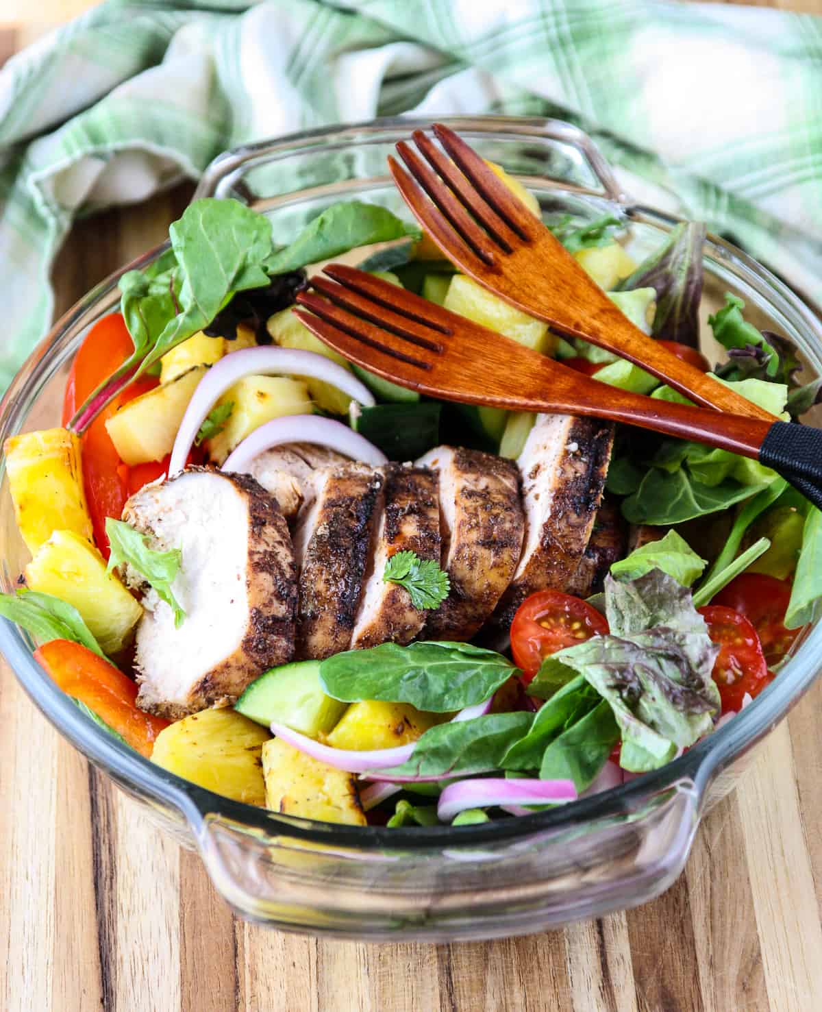 Jerk chicken salad in a glass bowl with two wooden salad forks.