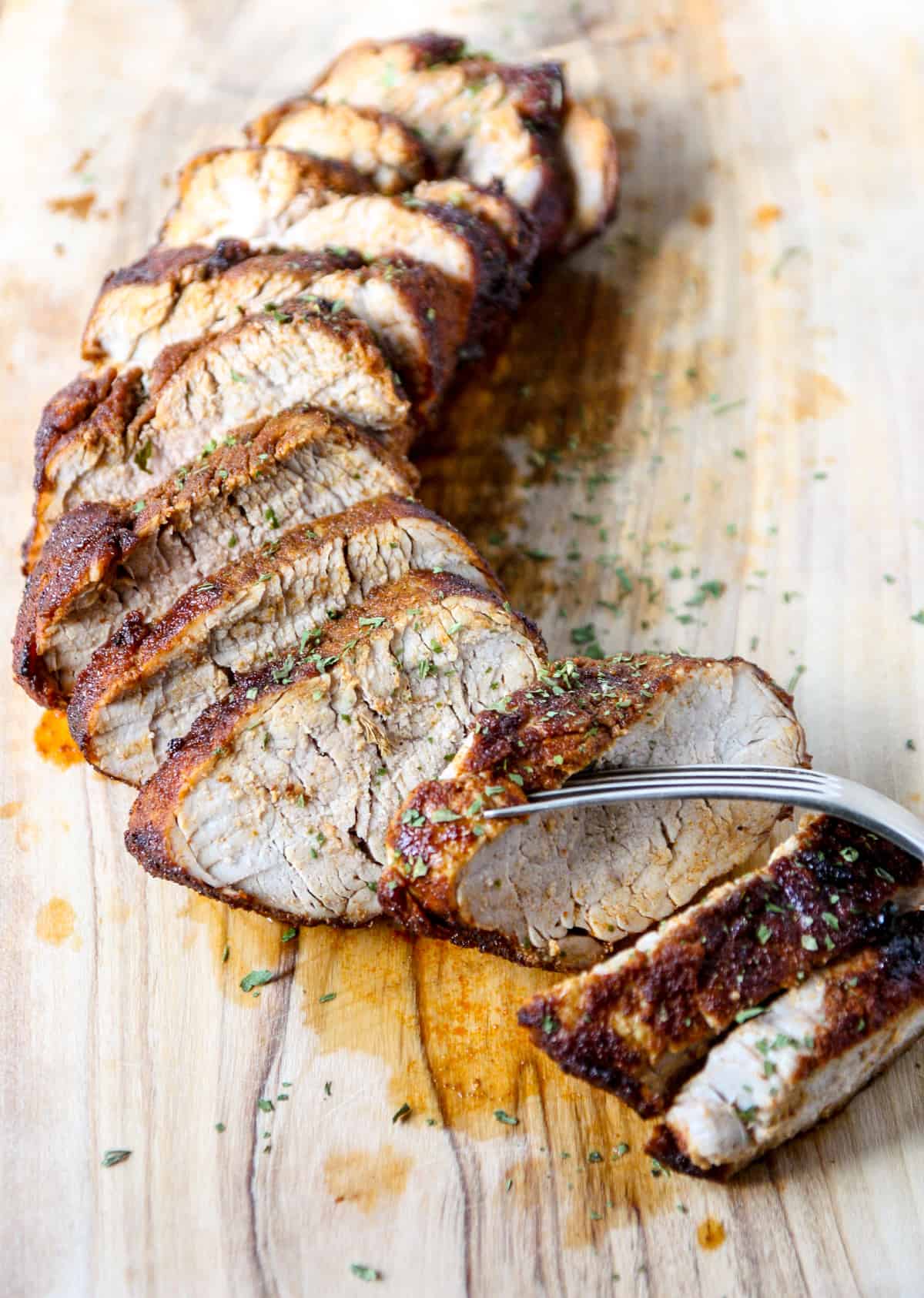 Slices of air fried pork tenderloin on a wooden cutting board.