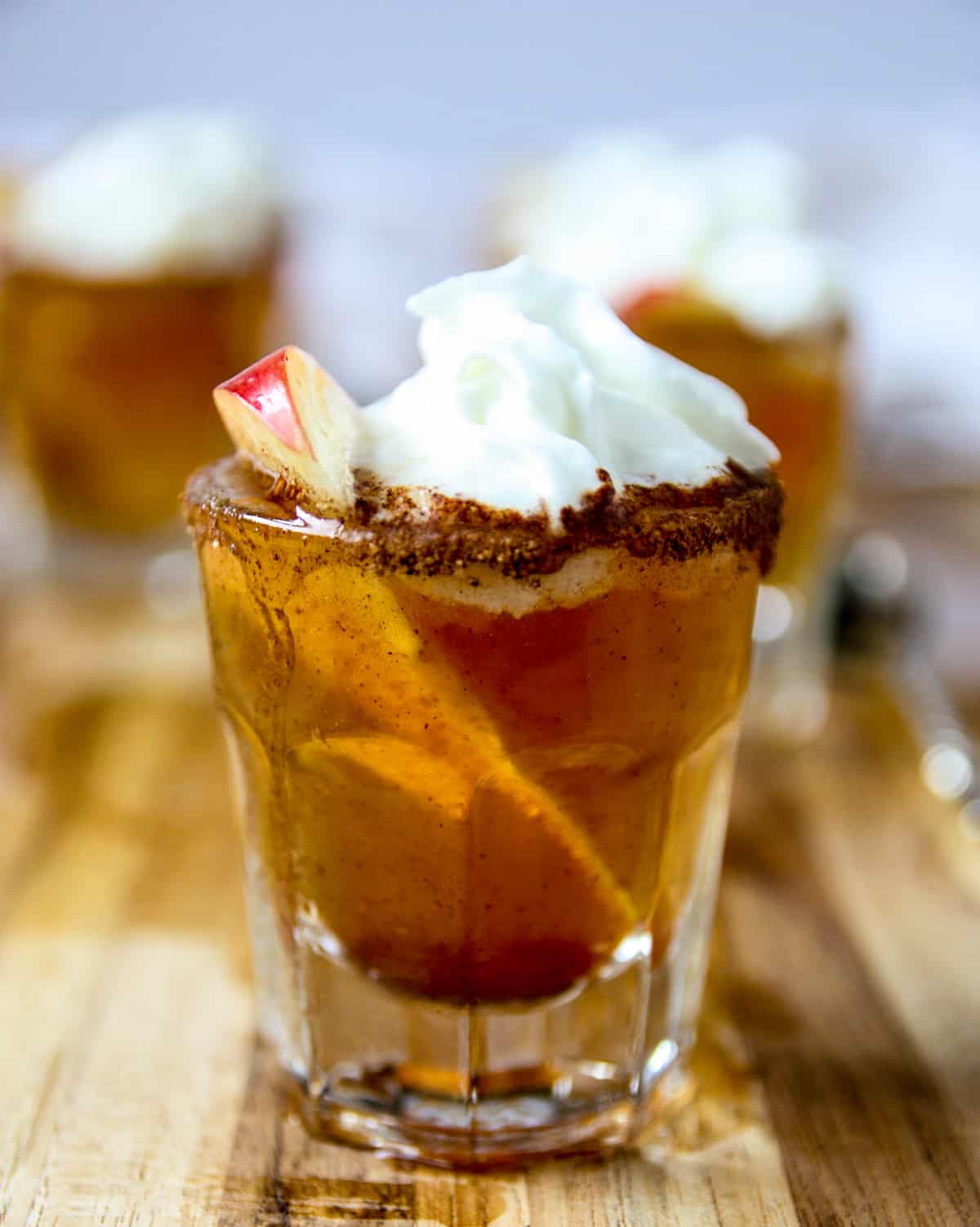An apple pie shooter topped with whipped cream.