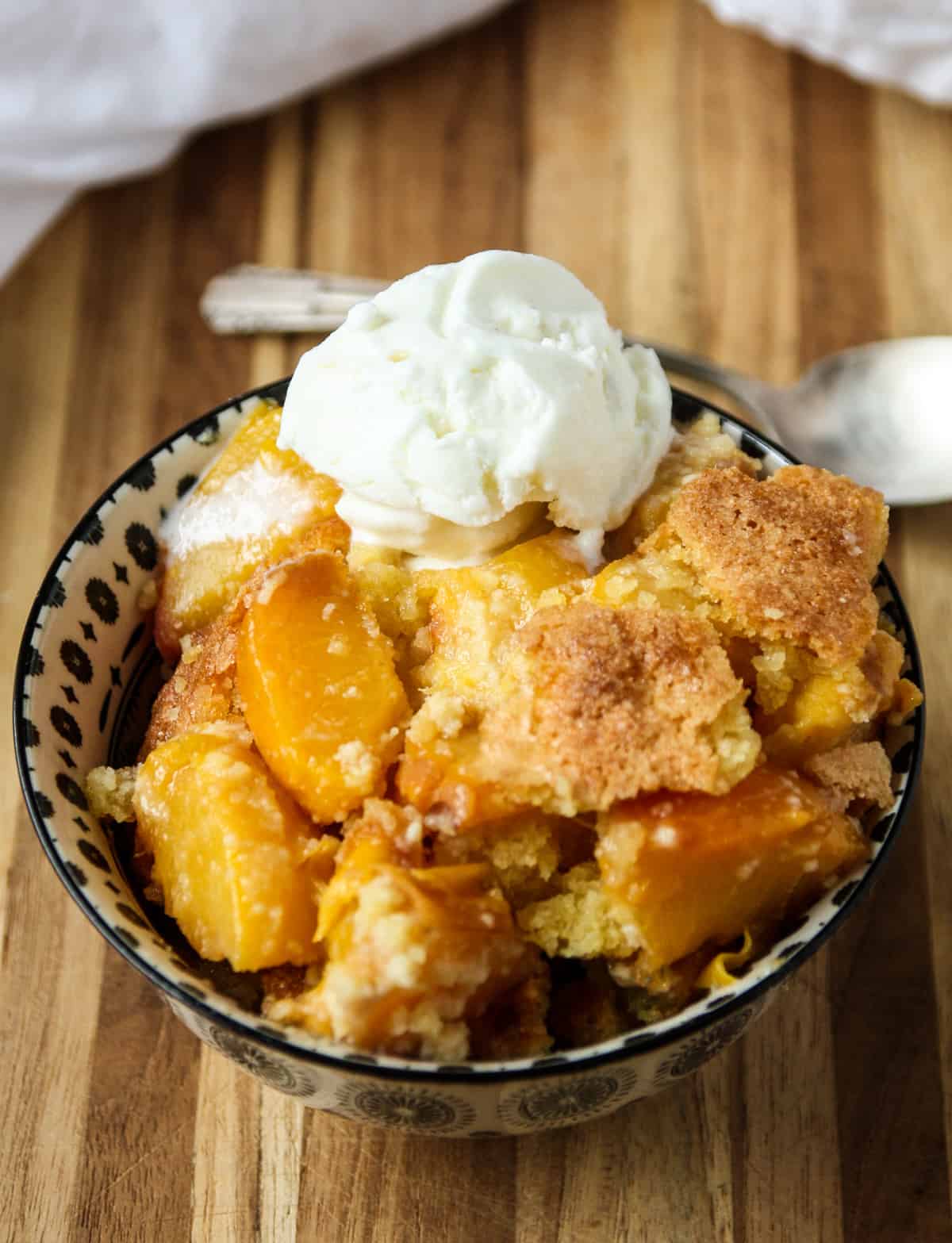 Peach cobbler topped with a scoop of ice cream in a black and white dish.