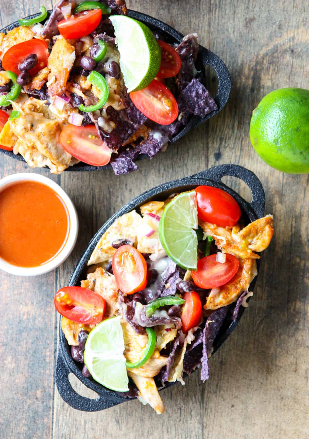 Two dishes of leftover turkey natchos with lime wedges.
