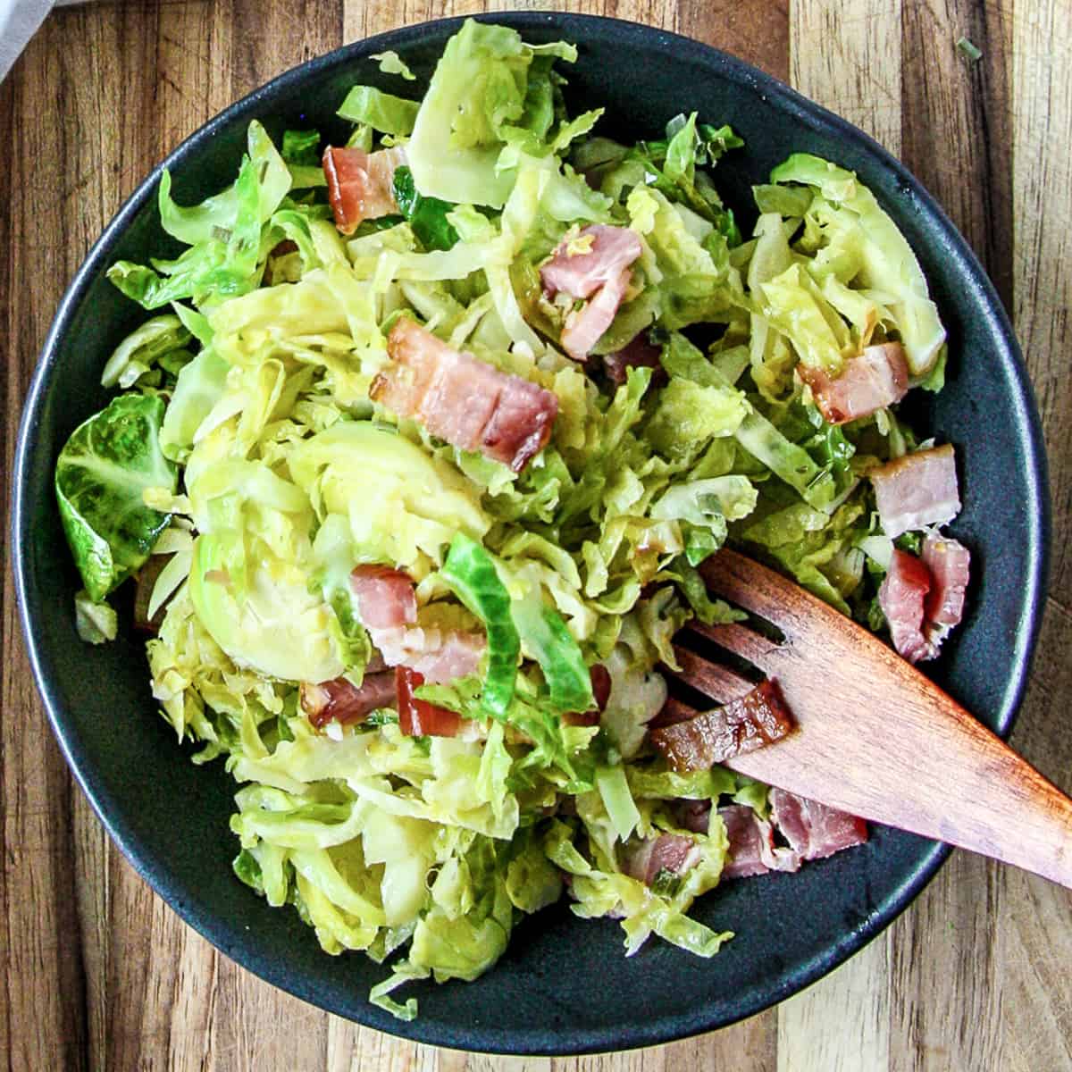 Shredded brussels sprouts with bacon in a black dish.