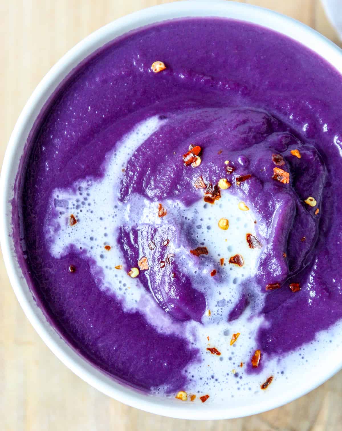 A bowl of red cabbage soup garnished with coconut cream and chili flakes.