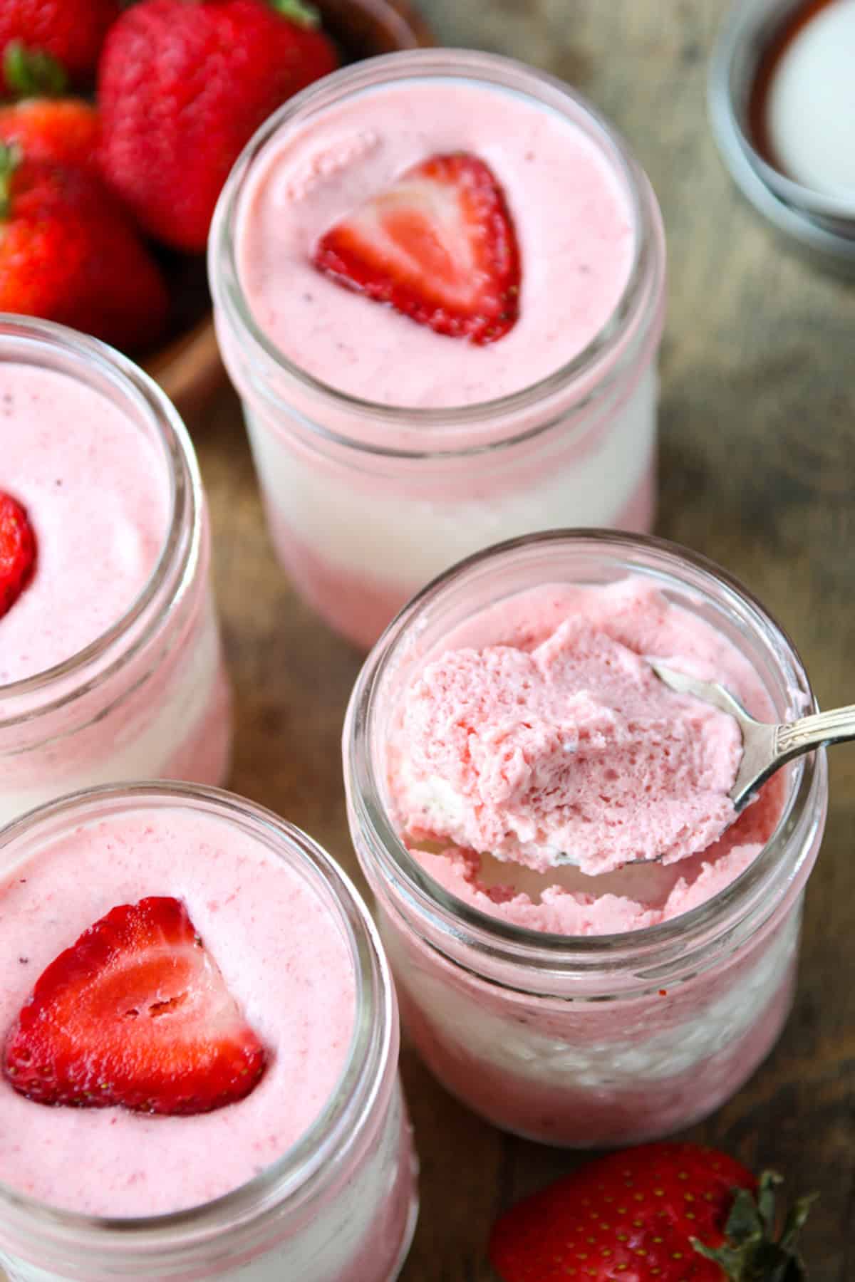 A spoonful of layered strawberry mousse being scooped from a jar.